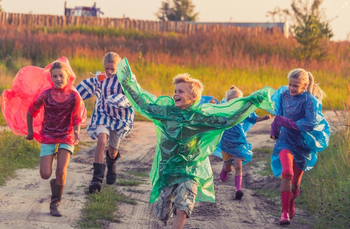 glada barn som springer med färgglad regnjacka